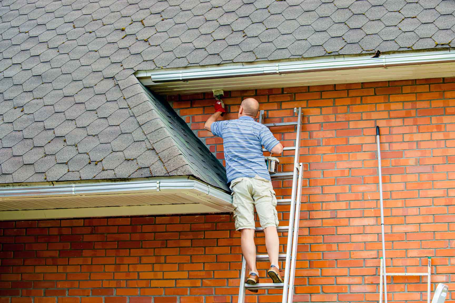 Mann auf Leiter bei der Arbeit an einer Hausfassade.