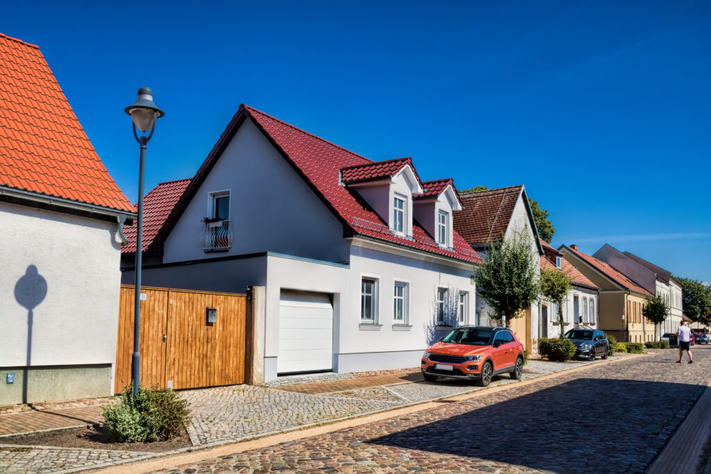 Haus an einer gepflasterten Straße, davor parkt ein Auto.