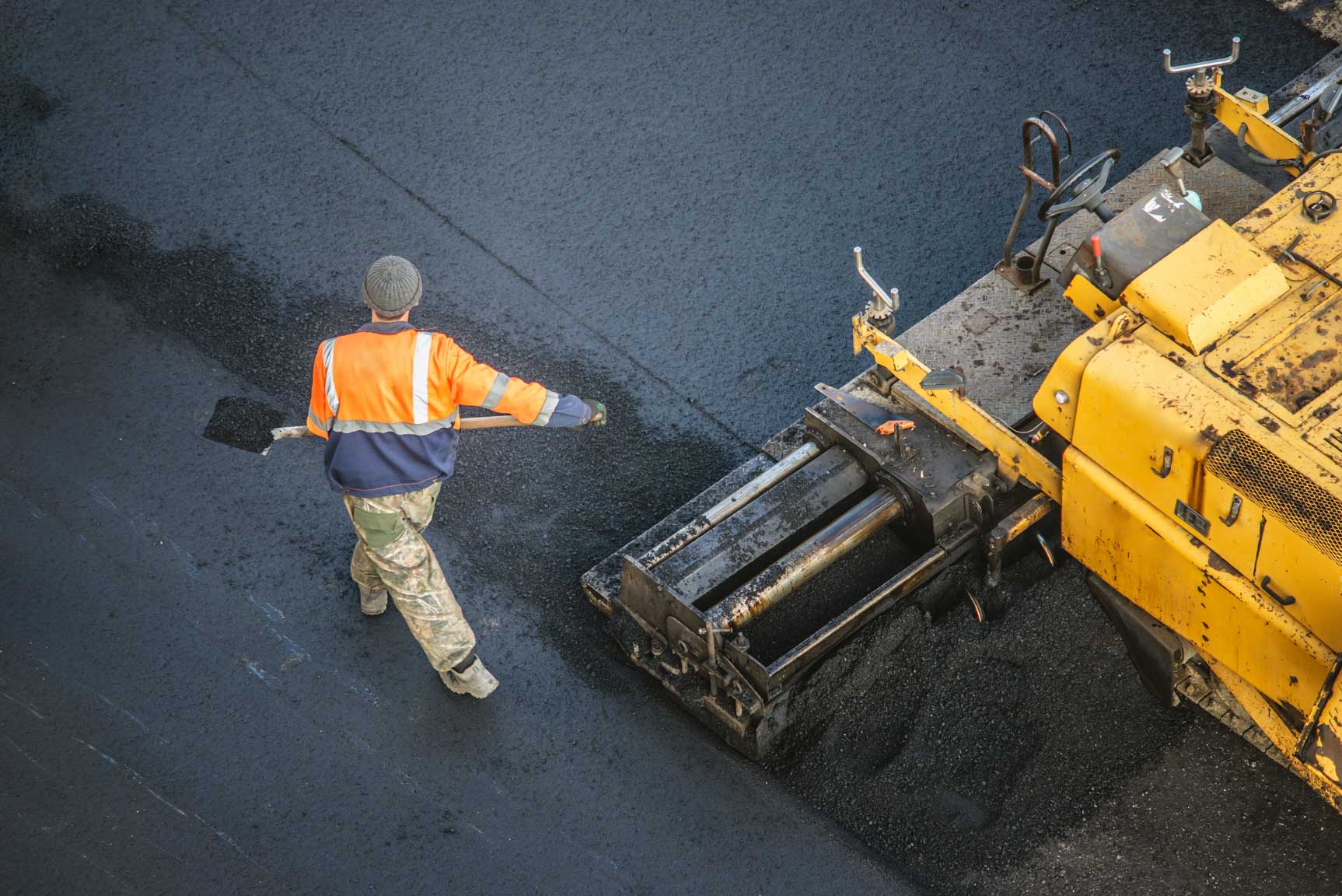 Bauarbeiter verteilt frischen Asphalt auf einer Stra&szlig;enfl&auml;che.