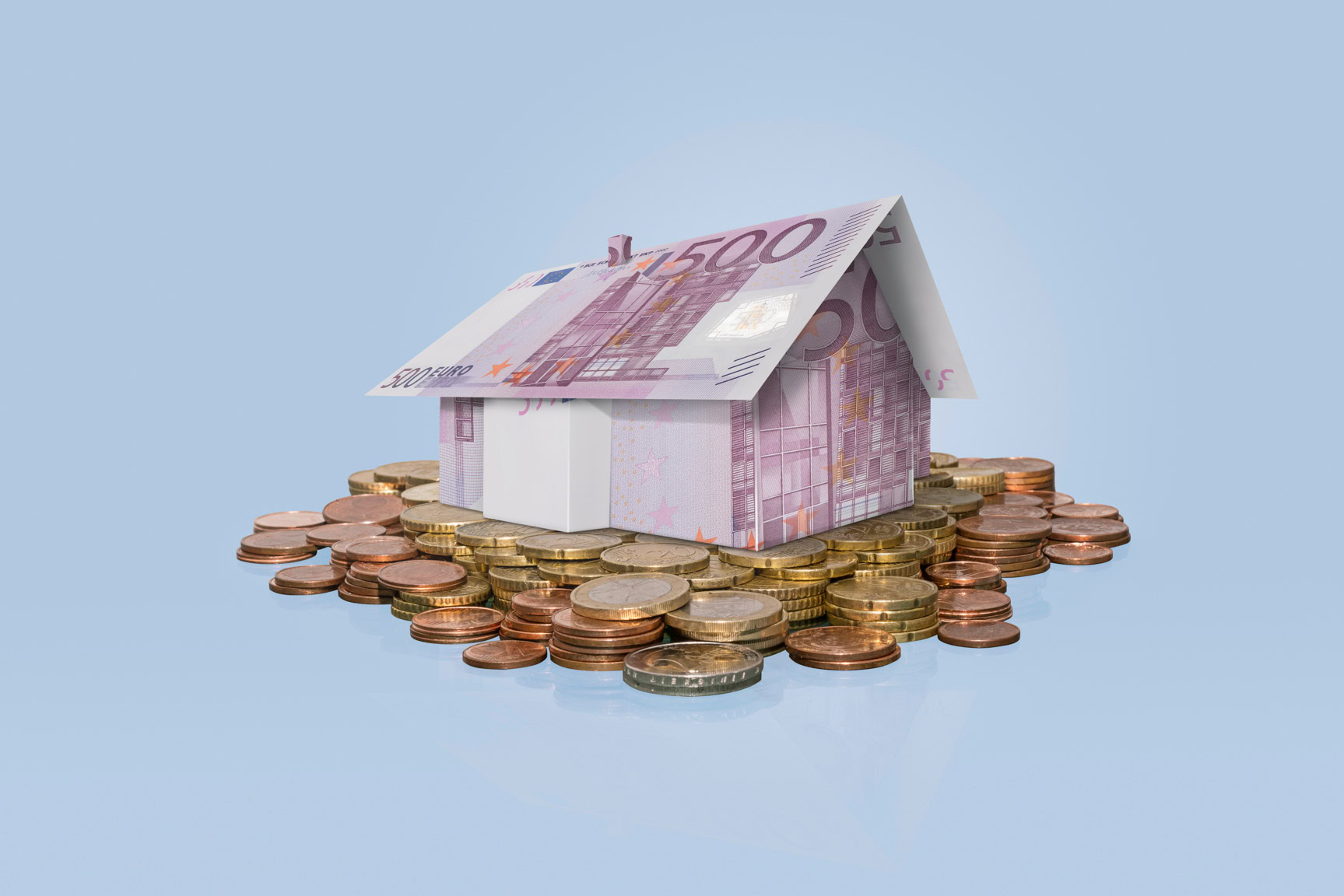 Hausmodell aus einem 500-Euro-Schein steht auf einem Stapel aus Euro-M&uuml;nzen vor hellem Hintergrund.
