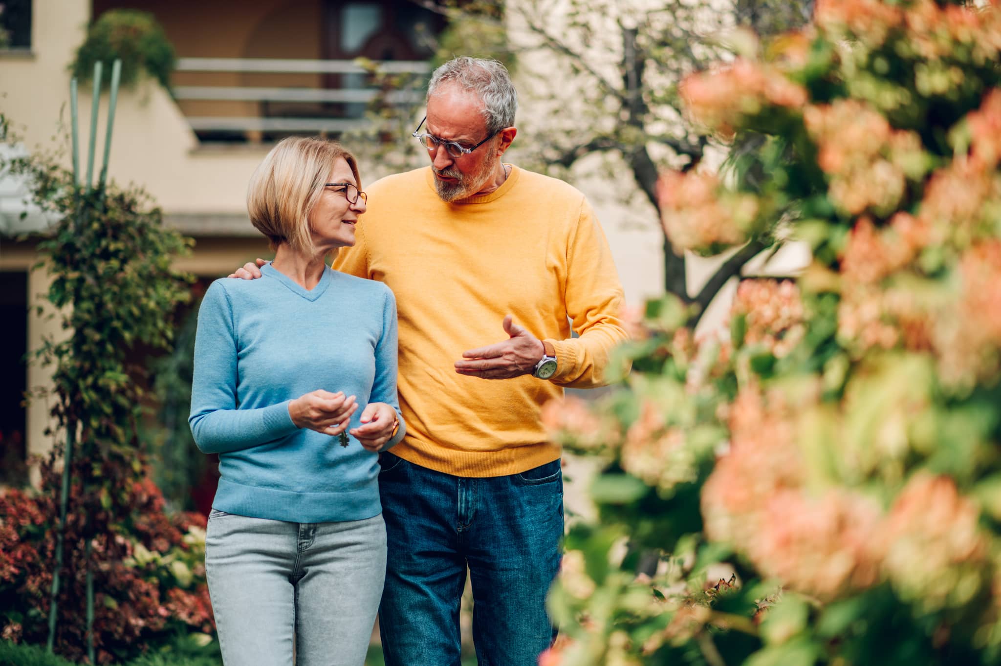 Älteres Paar im Gespräch über Zugewinngemeinschaft beim Erben im Garten vor einem Haus